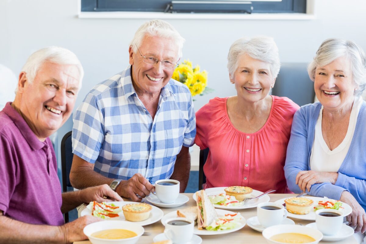 four smiling seniors sitting together at a table with food